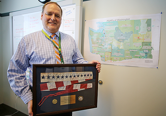 Adam Wasserman, wearing business attire, holds a Coast Guard pennant in a frame