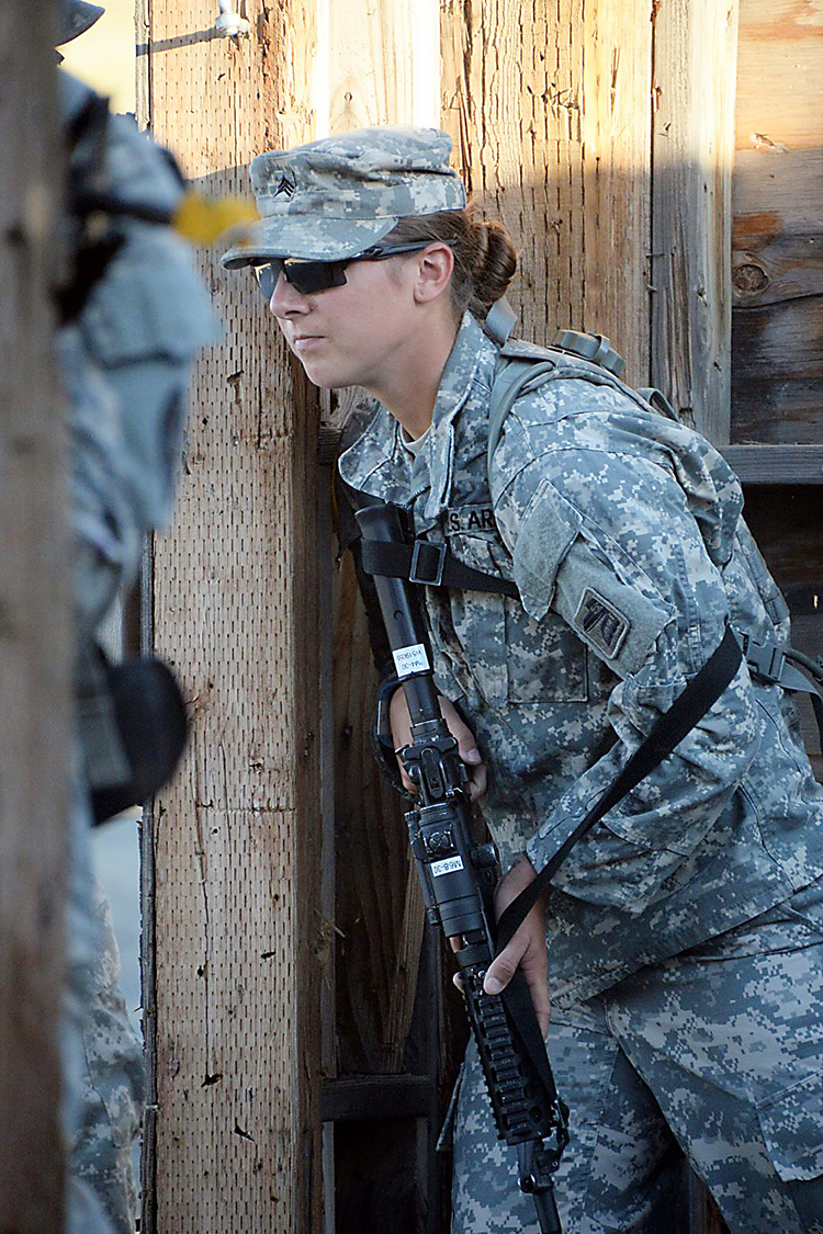 A female soldier holds a gun wearing camo and shades.